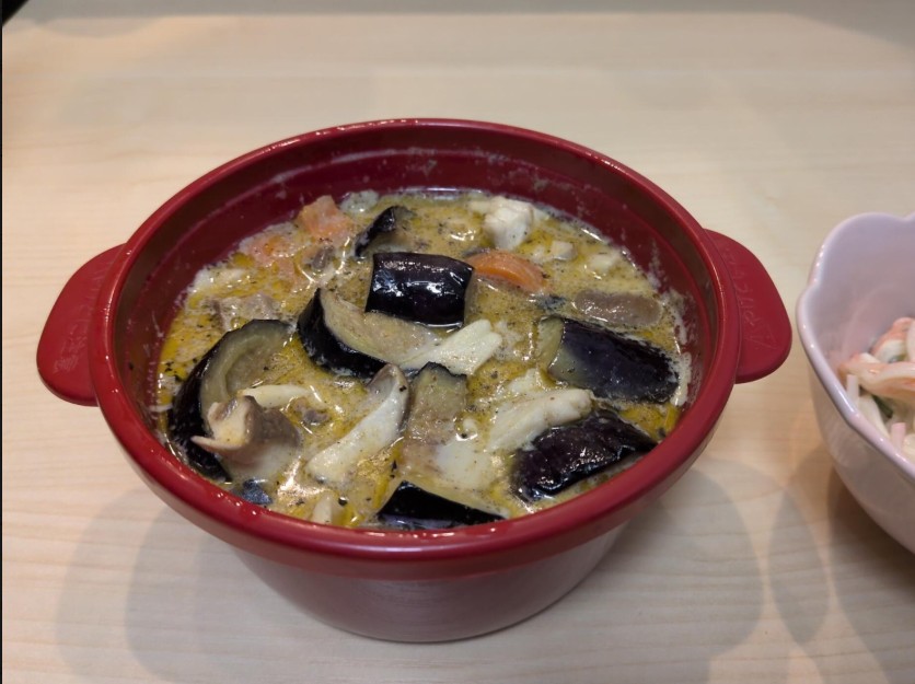 赤い鍋に入った鯖と茄子、きのこ、人参のグリーンカレー